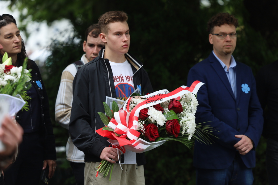 Uroczystość złożenia kwiatów pod Pomnikiem. Fotografia przedstawia mężczyznę trzymającego kwiaty.