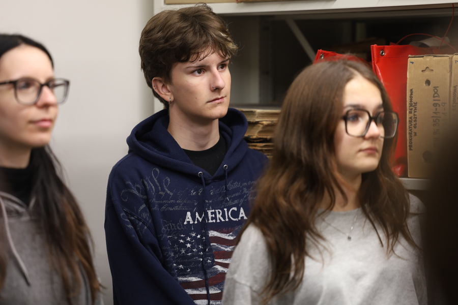 ZSEH Trzech uczniów stojących obok siebie podczas zajęć edukacyjnych. W centrum znajduje się uczeń w granatowej bluzie, po bokach dwie uczennice w okularach. Uczestnicy uważnie słuchają prowadzącego znajdującego się poza kadrem.