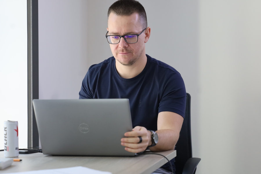 Prowadzący zajęcia siedzi przy stole i korzysta z laptopa podczas spotkania edukacyjnego z młodzieżą.