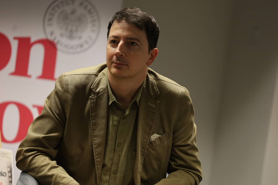 Dr Filip Gańczak siedzi w fotelu podczas spotkania z cyklu „Przystanek Historia”. W tle widoczny baner IPN.