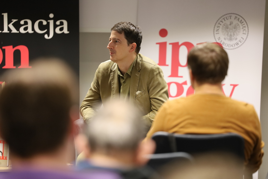 Dr Filip Gańczak siedzi w fotelu i zwraca się w stronę prowadzącego spotkanie. Na pierwszym planie widoczni uczestnicy wydarzenia.